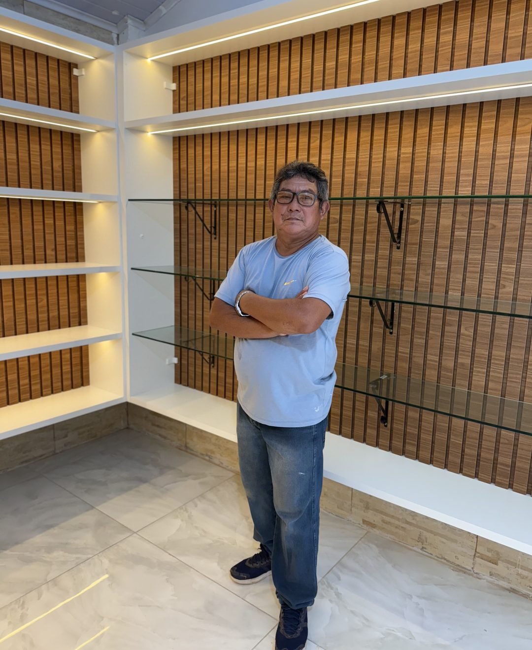 Edson Loureiro, marceneiro certificado pelo SENAI, ao lado de um painel ripado e prateleiras de vidro que projetou e instalou em Boa Vista, Roraima